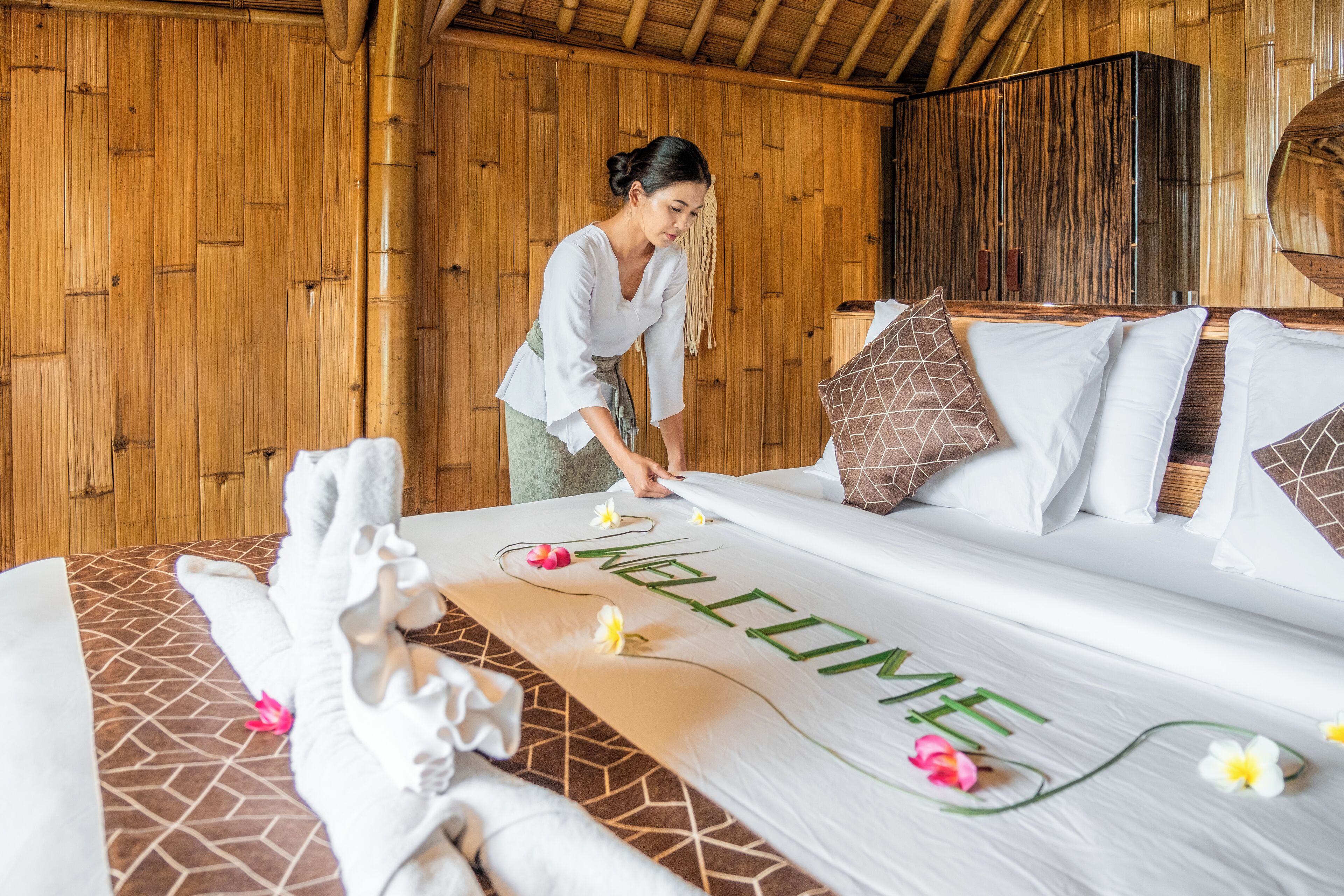 Ein ordentlich bezogenes Bett mit Fußmatte, Kissen und Blumen.