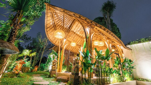 A bamboo structure with a thatched roof, surrounded by lush greenery and stone pathways. - Sindu Village Ubud (Ubud)