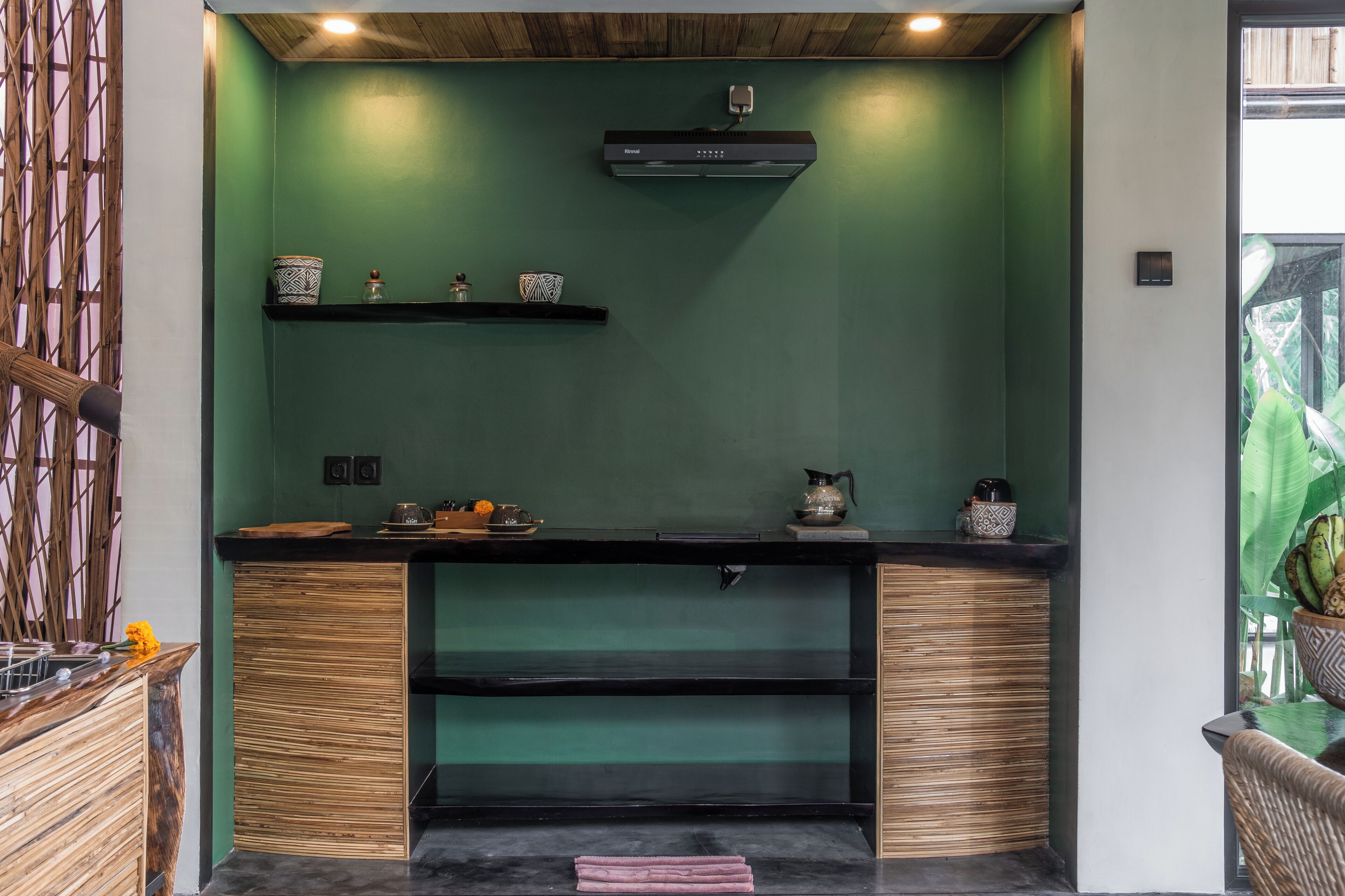 A kitchen with green walls, wooden cabinets, and a black countertop. There are shelves with decorative items and a coffee machine.