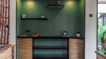 A kitchen with green walls, wooden cabinets, and a black countertop. There are shelves with decorative items and a coffee machine.