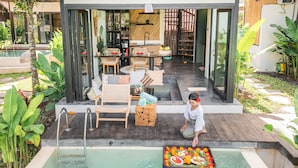 A pool area with a dining setup and a person arranging a fruit basket. - Sindu Village Ubud (Ubud)