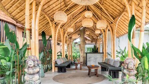 A covered outdoor area with bamboo ceiling, seating arrangements, and decorative statues. - Sindu Village Ubud (Ubud)