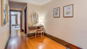 A hallway with wooden flooring, a desk with a chair, a mirror, and framed artwork on the wall. - Safe Area W/ Balcony - Great for Travel Nurses (Wichita)