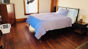 Un dormitorio con cama, cómoda de madera y ventana con cortina translúcida.