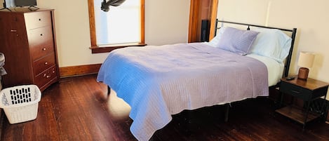A bedroom with a bed, wooden dresser, and a window with a sheer curtain.