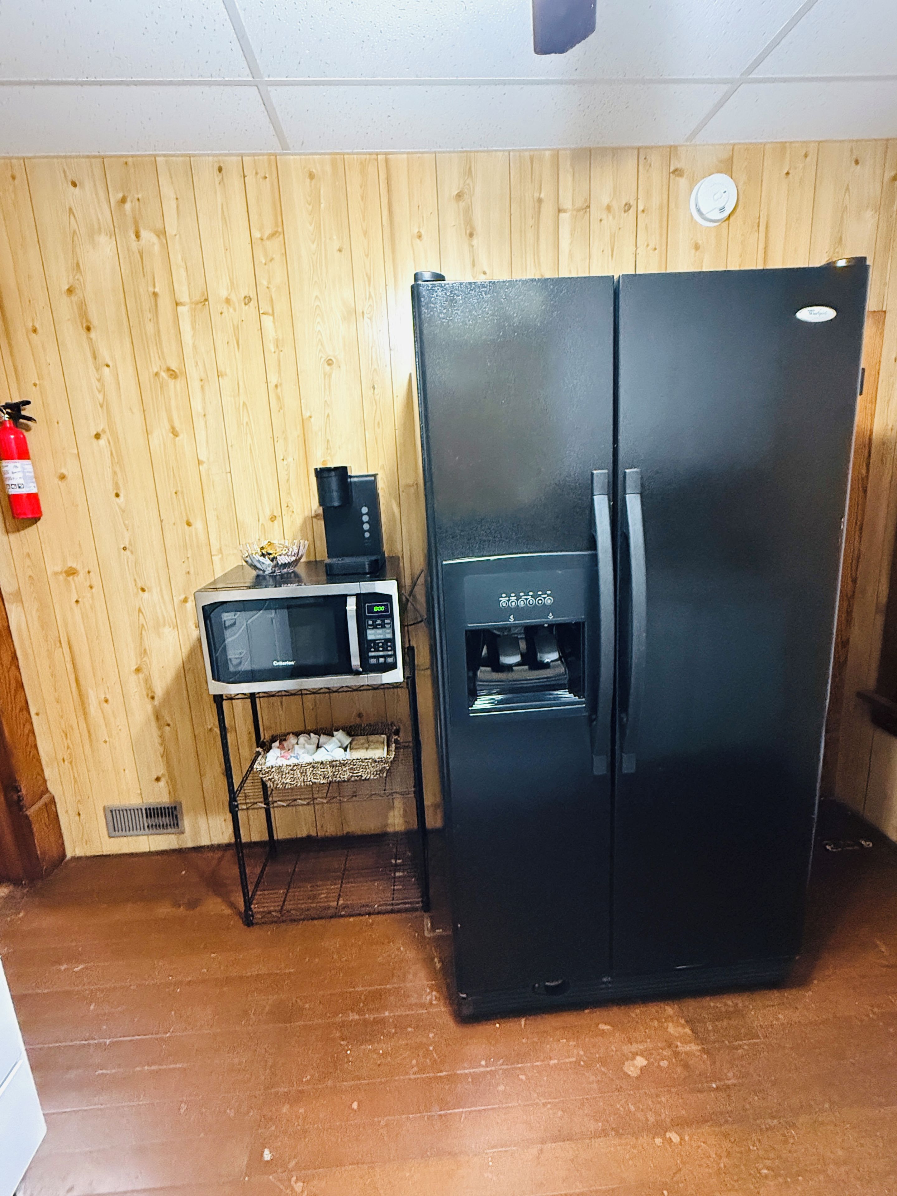 Eine Küche mit einem schwarzen Kühlschrank, einer Mikrowelle und einer Kaffeemaschine auf einer Holzausstattung.