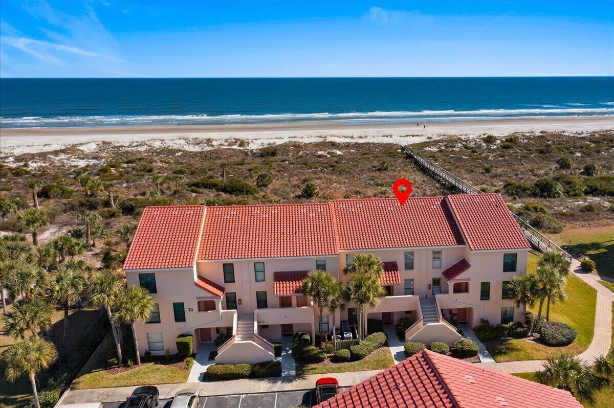 Um hotel com vários andares e telhado de telhas vermelhas, situado perto de uma praia com vista clara para o oceano.
