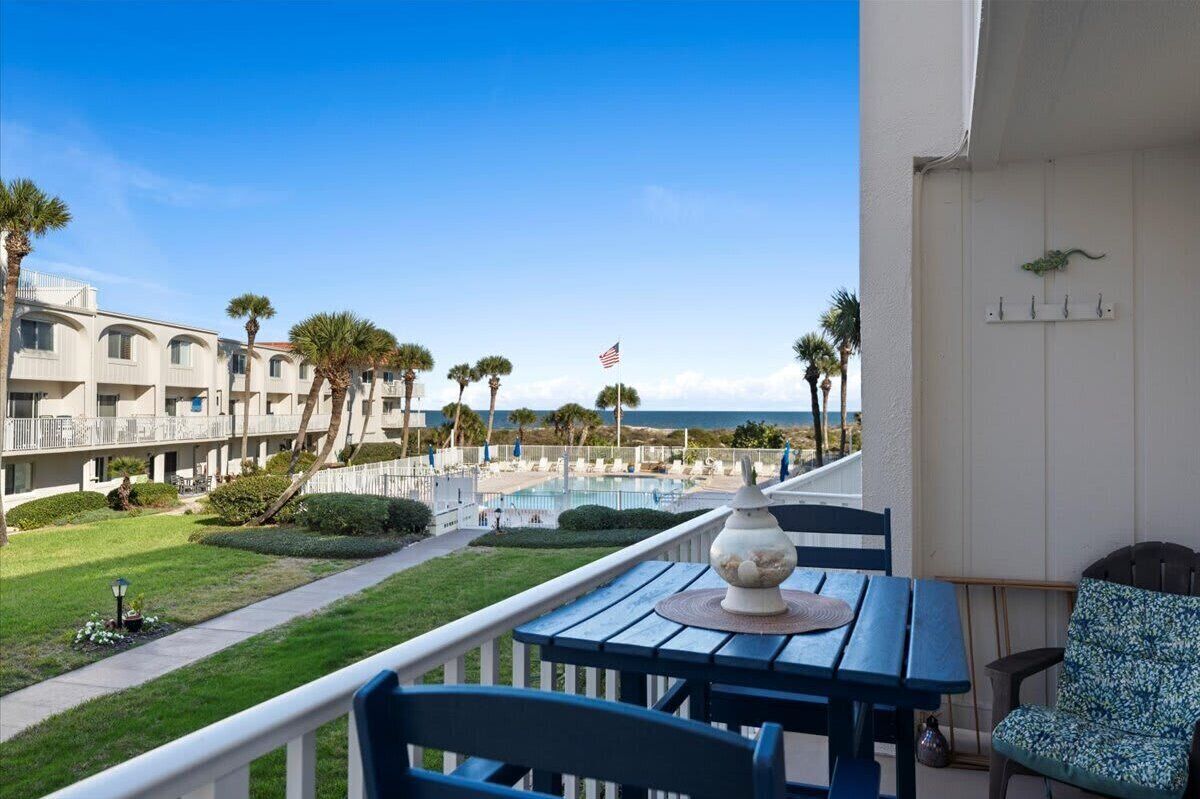 A balcony with a view of a swimming pool, palm trees, and a building with a flag.
