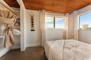 A bedroom with a wooden ceiling, a bed with a quilted cover, a hanging robe, and a wall-mounted decoration. - Friendship House | 5 Acres | Secluded | Hot Tub (Twentynine Palms)