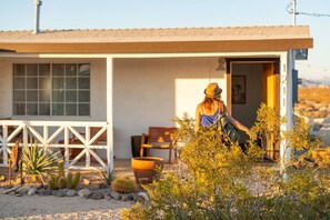 A single-story building with a covered porch, a dining area with a table and chairs, and a variety of desert plants. - Friendship House | 5 Acres | Secluded | Hot Tub (Twentynine Palms)