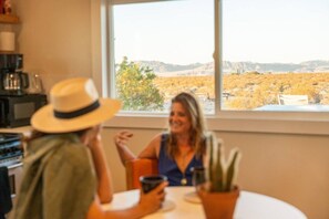 A dining area with a view of a desert landscape through a large window. - Friendship House | 5 Acres | Secluded | Hot Tub (Twentynine Palms)