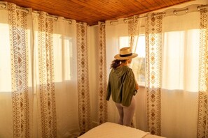 A room with patterned curtains, a bed, and a person standing by the window. - Friendship House | 5 Acres | Secluded | Hot Tub (Twentynine Palms)