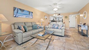 Ein Wohnzimmer mit zwei Sofas, einem Couchtisch, einem Deckenventilator und einem Gemälde mit Strandmotiv.