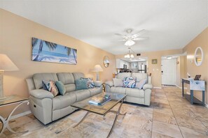 A living room with two sofas, a coffee table, a ceiling fan, and a painting of a beach scene. - Oceanfront 2BR Condo in St. Augustine (St. Augustine)