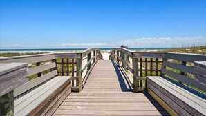 Ein hölzerner Steg führt zu einem Strand unter blauem Himmel.