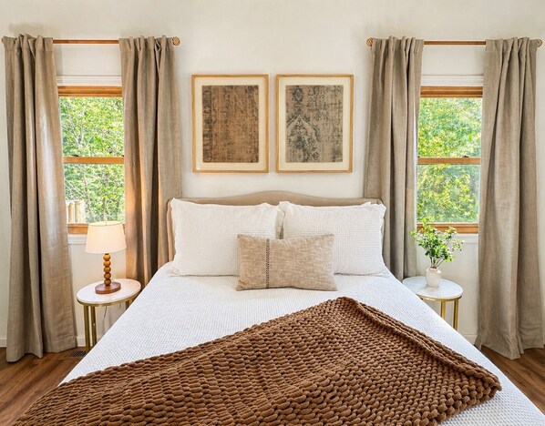 A bedroom with a bed, two framed pictures, a bedside table with a lamp, and a window with curtains. - Private Pool Retreat- Fire Table + Country Escape in Cleveland TN (Cleveland)