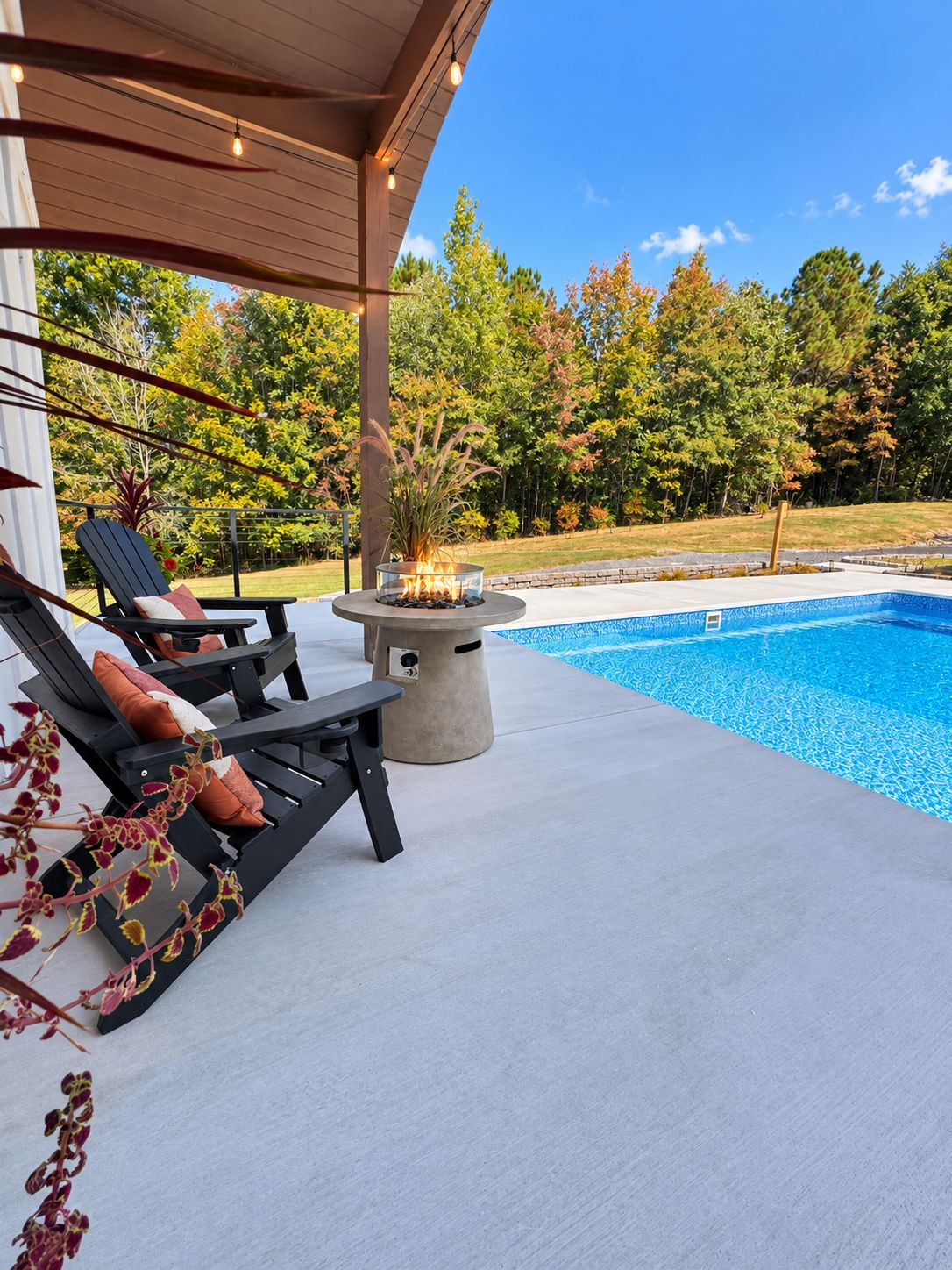A poolside area with lounge chairs, a fire pit, and a view of a swimming pool.