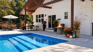 Ein Swimmingpool mit überdachter Terrasse, Sitzgelegenheiten im Freien und Blumentöpfen.