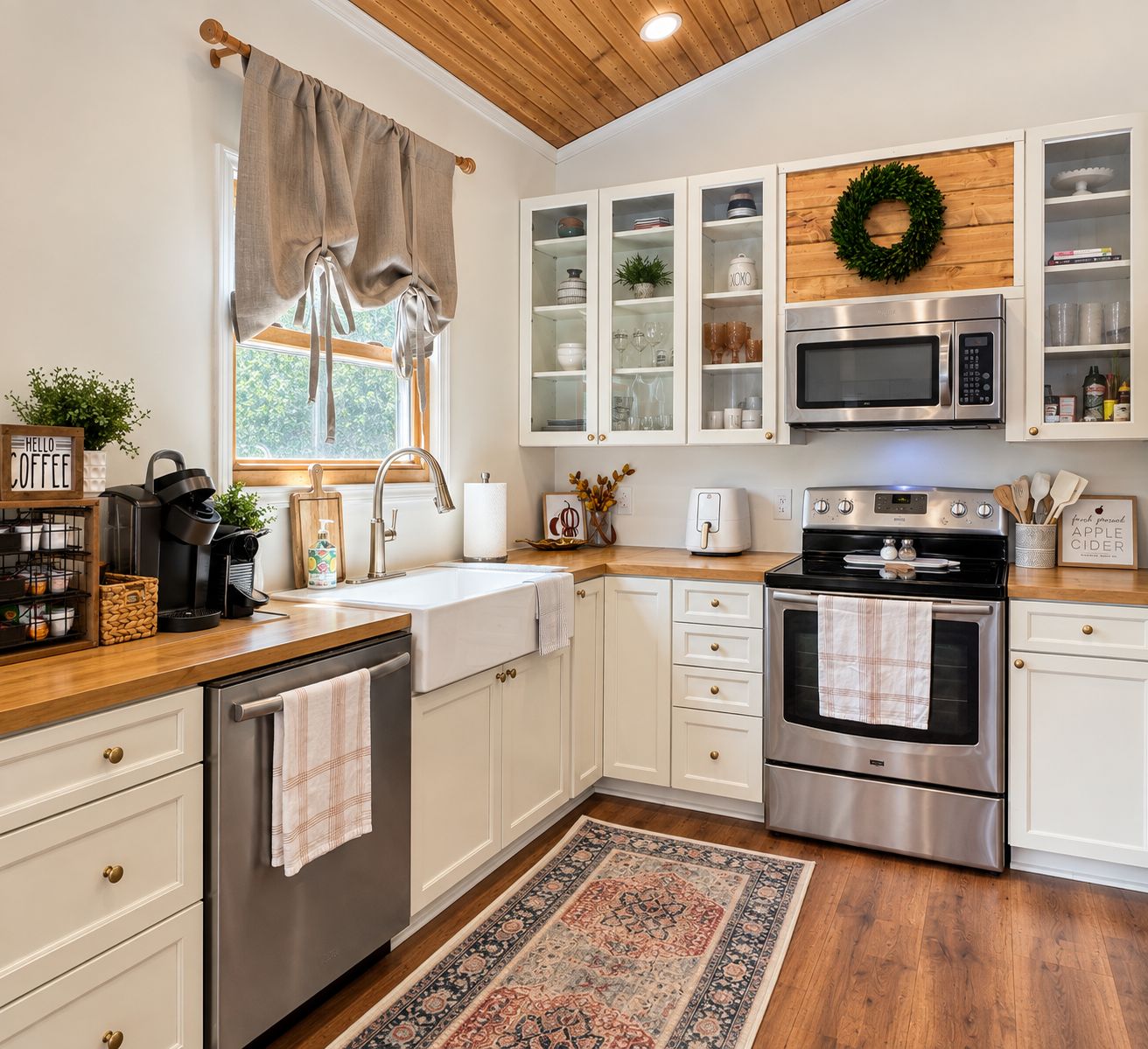 A kitchen with white cabinets, stainless steel appliances, a wooden ceiling, and a window with curtains.