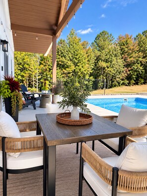 An outdoor patio with a table and chairs, a potted plant, and a swimming pool in the background. - Private Pool Retreat- Fire Table + Country Escape in Cleveland TN (Cleveland)