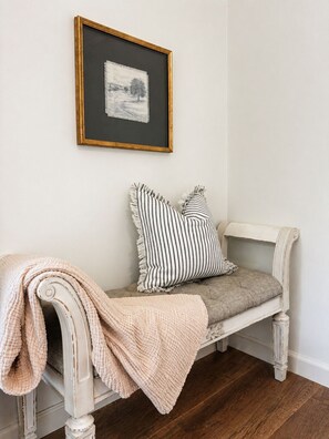A white bench with a cushion and a throw blanket, a framed picture on the wall, and a wooden floor. - Private Pool Retreat- Fire Table + Country Escape in Cleveland TN (Cleveland)