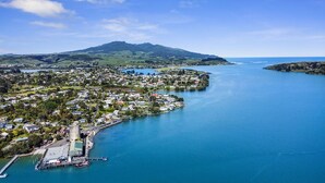 An aerial view of a coastal town with a marina, residential areas, and a prominent hill in the background. - Iconic property • Spectacular outlook (Raglan)