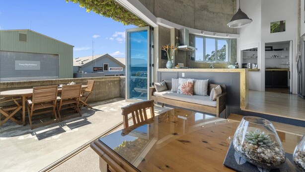 A modern kitchen with a large island, a dining area with wooden furniture, and a view of the sea. - Iconic property • Spectacular outlook (Raglan)