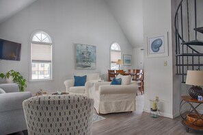 A spacious living room with a high ceiling, white walls, and a staircase. There are two white sofas, a patterned armchair, and a dining area with wooden chairs. - Family-Friendly Wells, Maine Vacation Home Near Ogunquit & Beaches (Wells)