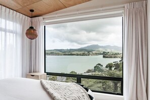 A bedroom with a large window offering a view of a lake and hills. - On Point House • Upstairs • Luxury Design (Raglan)