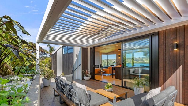 Un área de estar al aire libre moderna con terraza de madera, asientos acolchados y plantas en macetas.