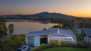 Una casa moderna con un amplio ventanal de vidrio, rodeada de exuberante vegetación y un lago.