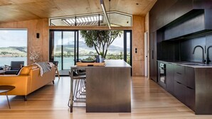 Una cocina moderna con una isla grande, armarios oscuros y vistas a un lago y colinas.