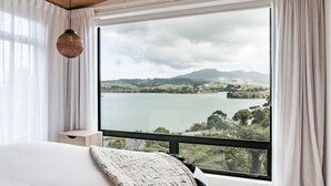 Un dormitorio con un ventanal que ofrece vistas a un lago y colinas.