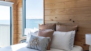 Ein Schlafzimmer mit einem hölzernen Kopfteil, einem Bett mit weißer Bettwäsche und Meerblick durch ein großes Fenster.