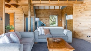 Ein gemütliches Cabin-Interieur mit einer grauen Couch, einem Holztisch und Blick ins Grüne durch ein Fenster.