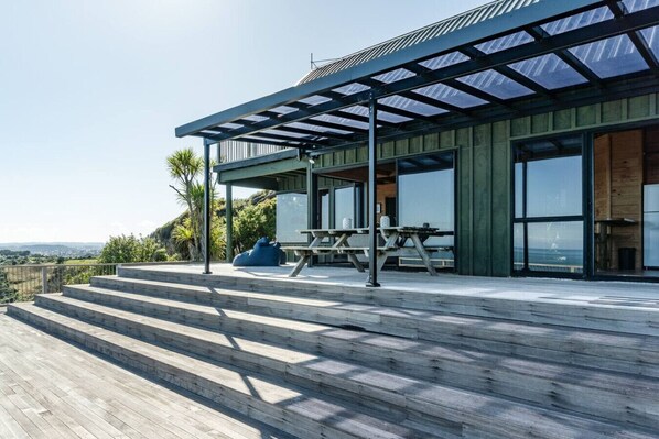 A modern house with a wooden deck, large windows, and a covered outdoor area.