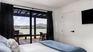 Ein Schlafzimmer mit Bett, einem an der Wand montierten Fernseher und Seeblick durch große Fenster.
