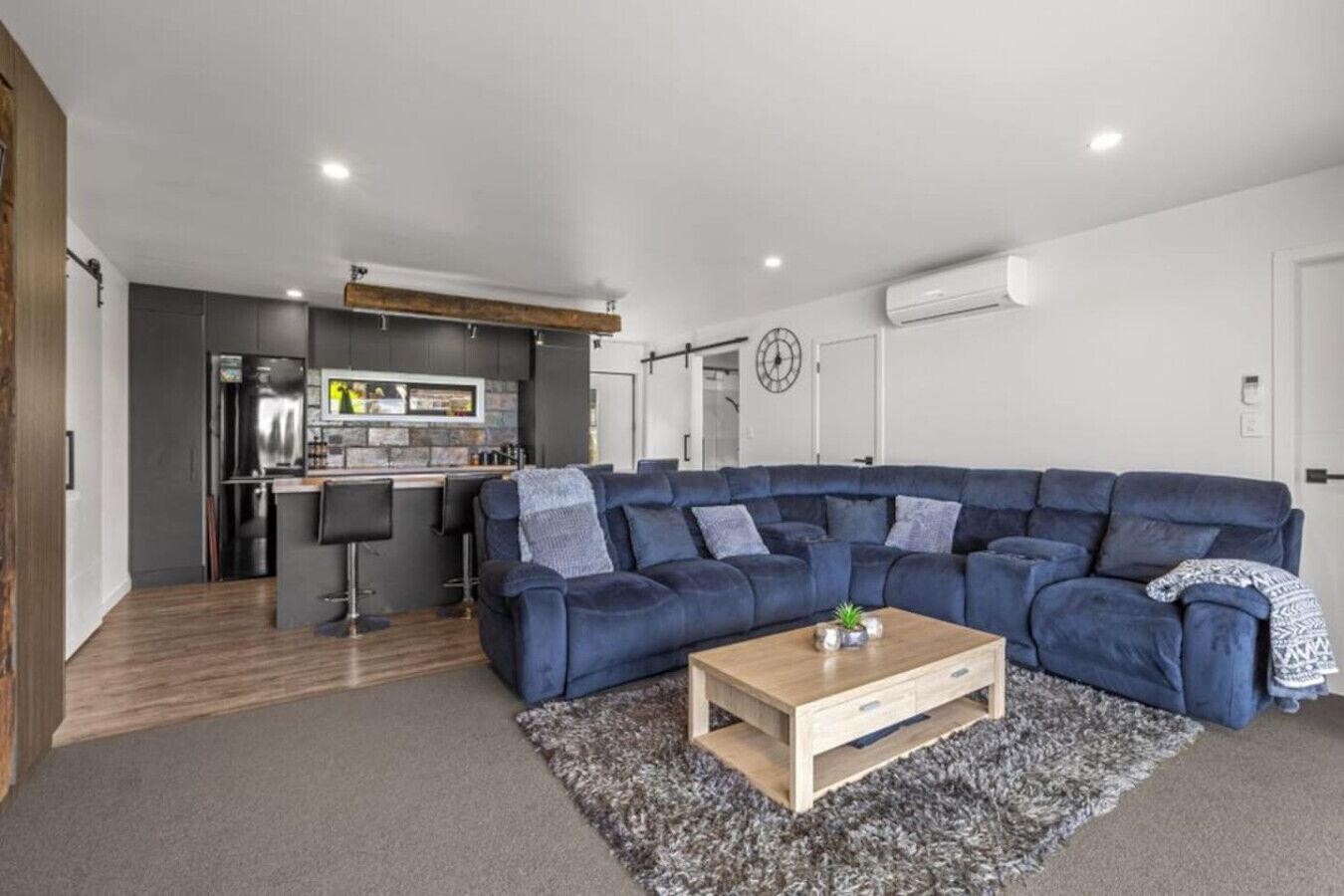 A modern living room with a large blue sectional sofa, a wooden coffee table, and a grey shag rug.