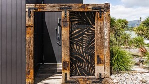 Ein rustikales Holztor mit einem Metallriegel, das zu einem modernen Gebäude mit dunkler Fassade führt.