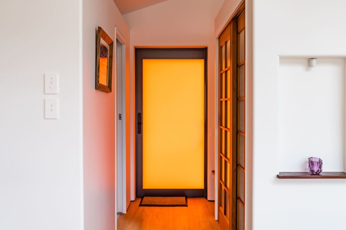 A hallway with a wooden door leading to a room with a bright orange interior.