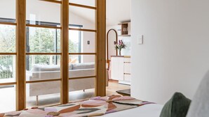 Quarto com uma janela ampla, cama com colcha florida, e vista para uma varanda com sofá.