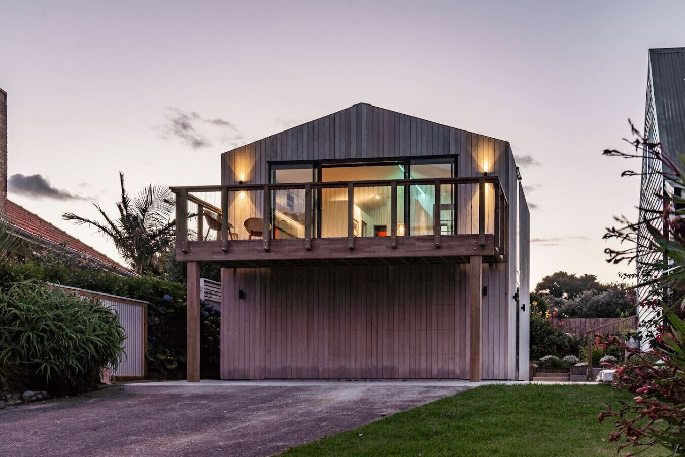 A modern two-story house with a balcony, a visible staircase, and a well-maintained garden.