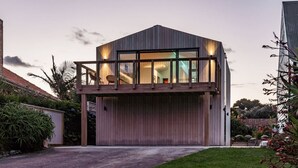 Uma casa moderna de dois andares com varanda, escada visível e um jardim bem cuidado.