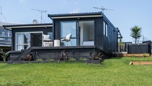 Uma casa moderna de cor escura, com uma grande porta de vidro que dá para um quarto, uma pequena varanda com duas cadeiras e uma antena parabólica no telhado.