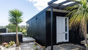 Um edifício moderno preto com porta branca, rodeado por um jardim com palmeiras e um espaço de pátio.