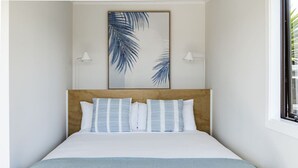Cama bem arrumada com cabeceira de madeira, roupa de cama branca e almofada listrada em azul.