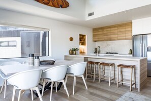 Una cocina moderna con una isla central, taburetes de bar y un comedor con sillas blancas.