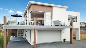 Ein modernes, zweistöckiges Haus mit flachem Dach, großen Fenstern und einer überdachten Terrasse.
