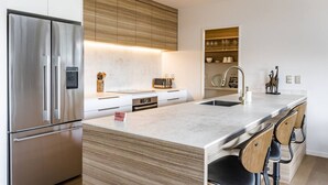 A modern kitchen with a stainless steel refrigerator, wooden cabinets, a marble countertop, and a built-in sink. - Okiwi Landing • Stylish • Central (Raglan)