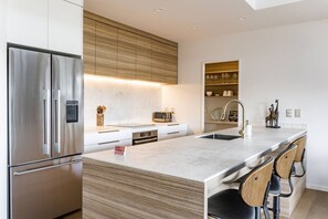 A modern kitchen with a stainless steel refrigerator, wooden cabinets, a marble countertop, and a built-in sink. - Okiwi Landing • Stylish • Central (Raglan)